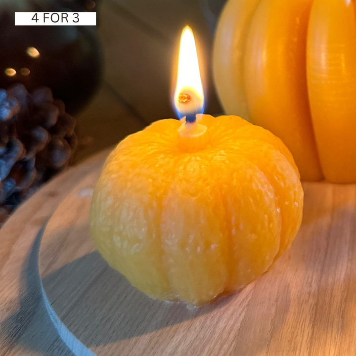 Lit handmade mini beeswax pumpkin candle glowing in an autumn display