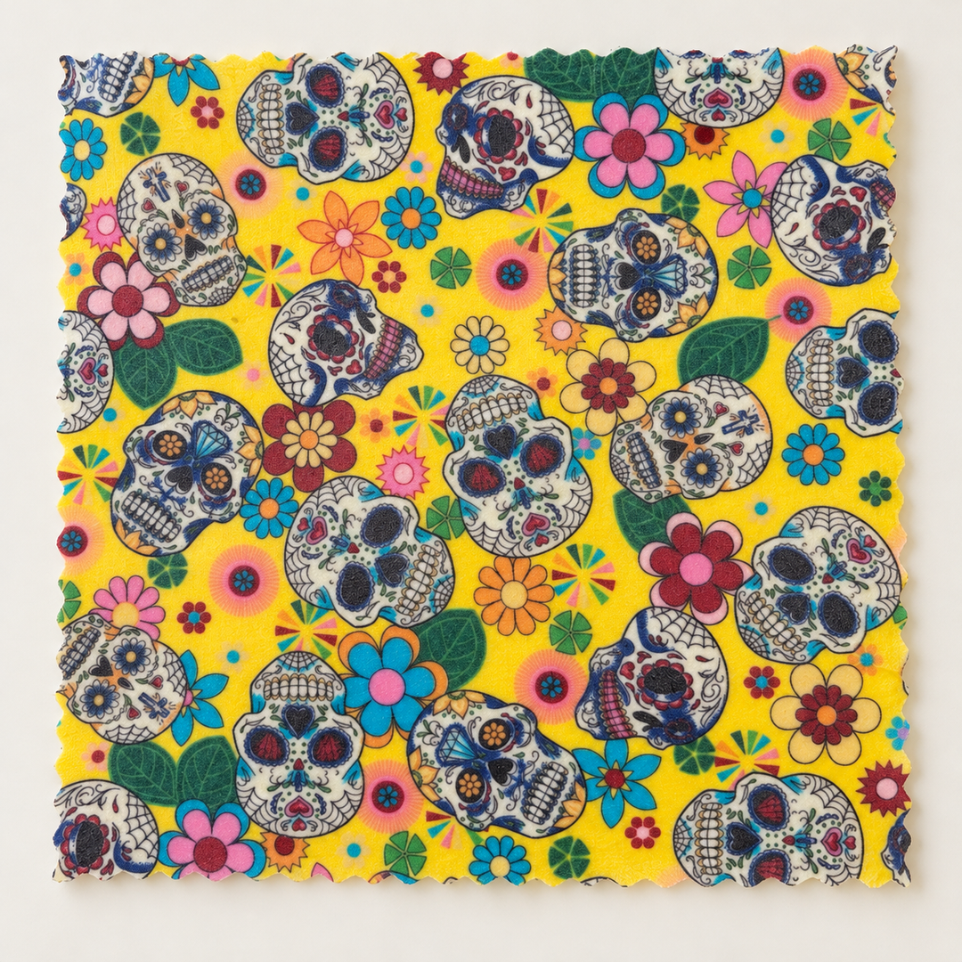 Yellow reusable beeswax food wrap with decorative skulls, colourful flowers and green leaves.