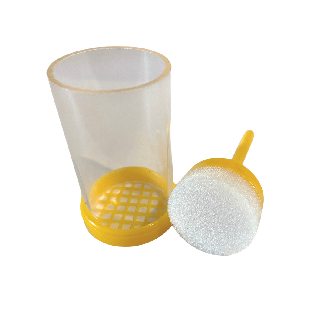 A yellow plastic queen bee marker cage with a clear tube and a yellow plunger with a white sponge pad.